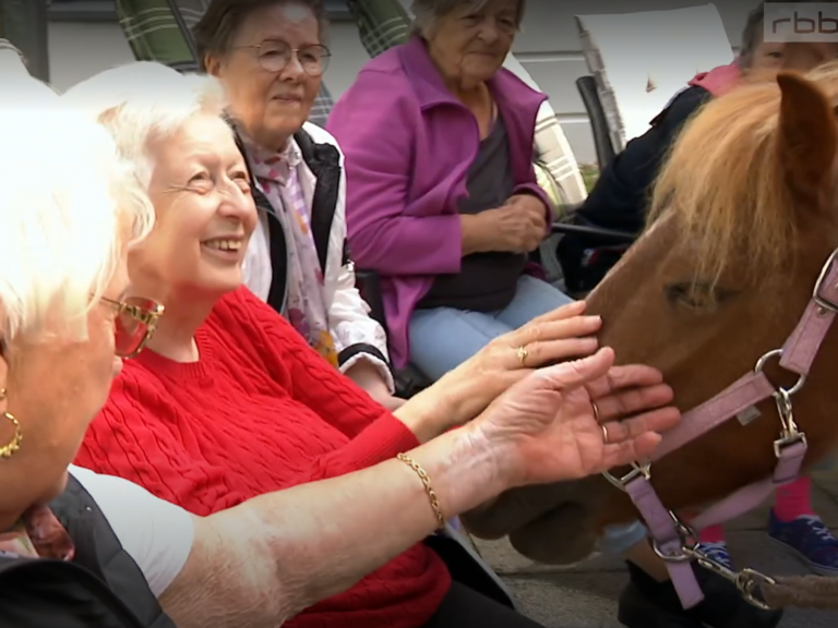 Screenshot aus der Sendung des rbb mit zwei Bewohnerinnen, die das Pony am Kopf streicheln Screenshot aus der Sendung des rbb mit zwei Bewohnerinnen, die das Pony am Kopf streicheln